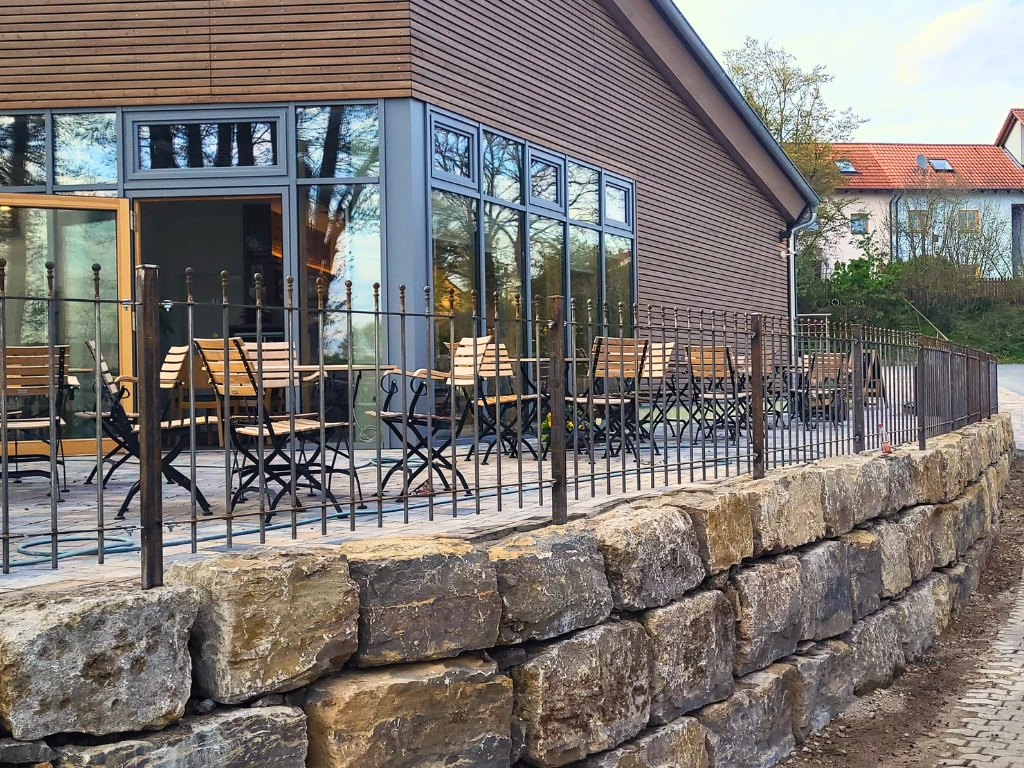 Natursteinmauer mit Geländer vor Terrasse eines Holzhauses