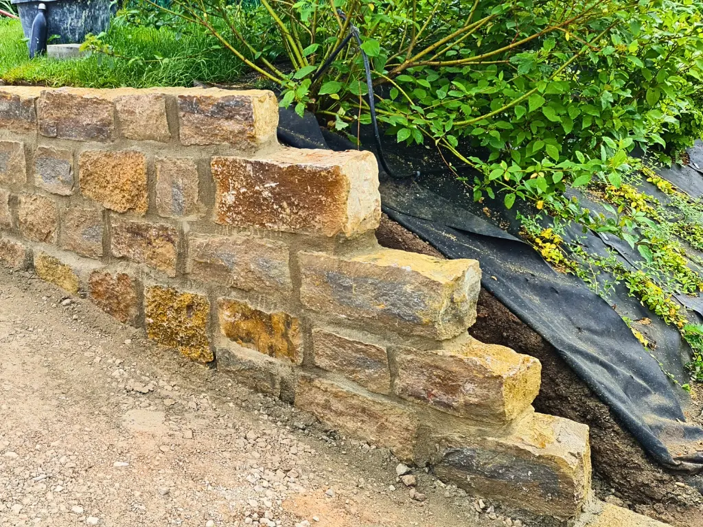 Kleinformatige Natursteinmauer mit Pflanzbereich im Garten