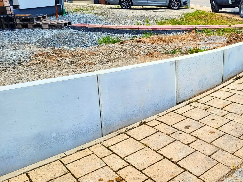 Leicht gebogene Betonmauer aus Mauerscheiben an Grundstücksgrenze